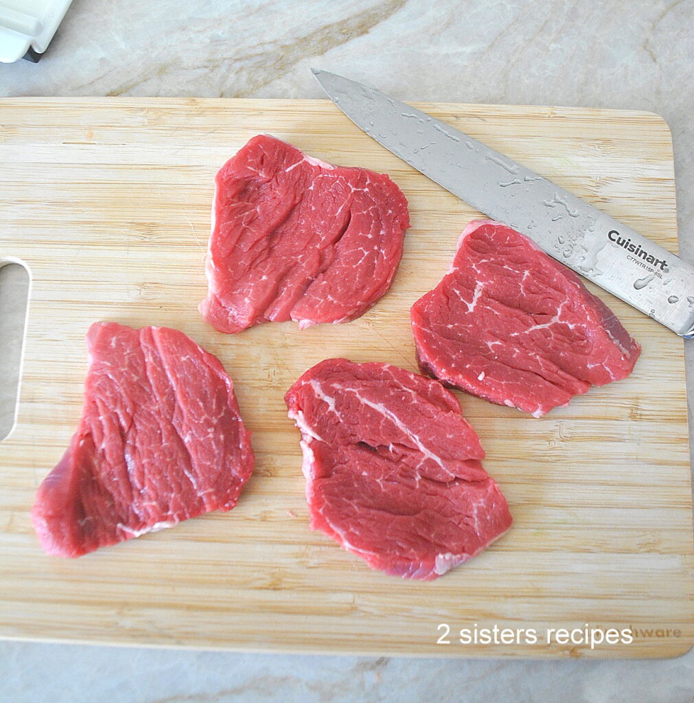 Four thinly sliced filet mignon on a wood cutting board.