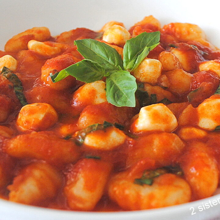 A white dish filled with gnocchi pasta smothered in tomato sauce with pearl mozzarella and basil.