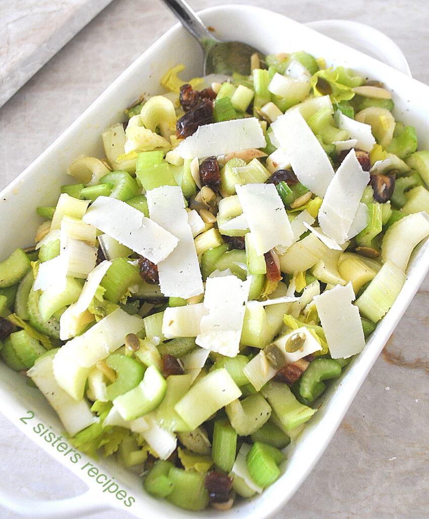A rectangular serving bowl filled with a celery salad with cheese shavings on top.