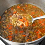 A large spoon filled with a beef barley vegetable soup.