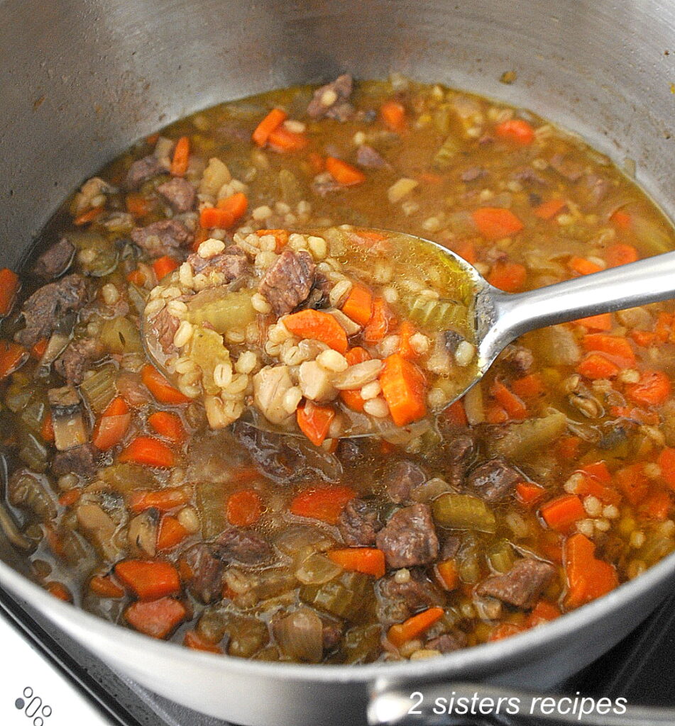 A large spoon filled with a beef barley vegetable soup.