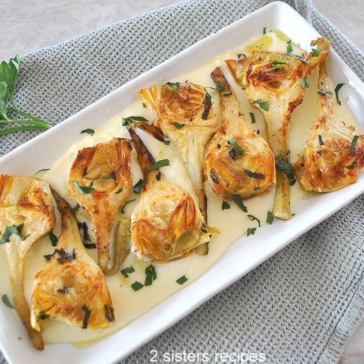 A rectangular dish with a serving of seared artichokes with stems over a cheese cream.