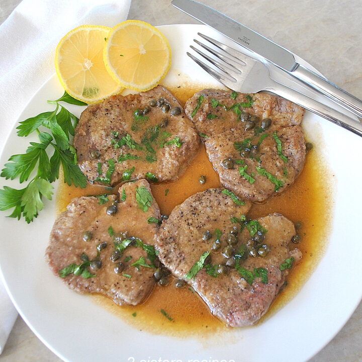Four seared thin steaks served on a white dinner plate with lemon-buttery sauce.