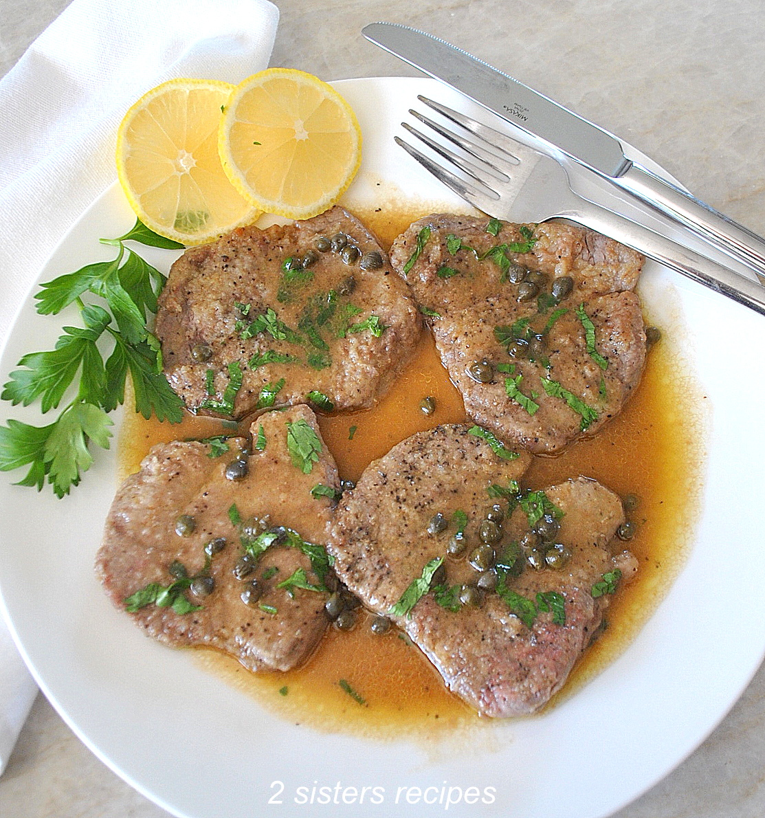 Four seared thin steaks served on a white dinner plate with lemon-buttery sauce.