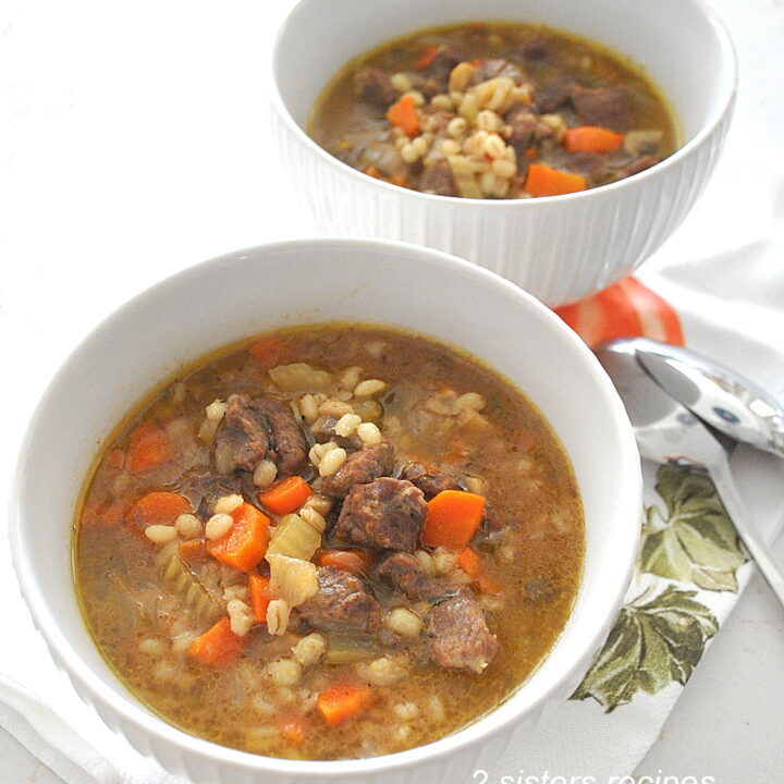 Two white bowls filled with a beef barley vegetable soup.