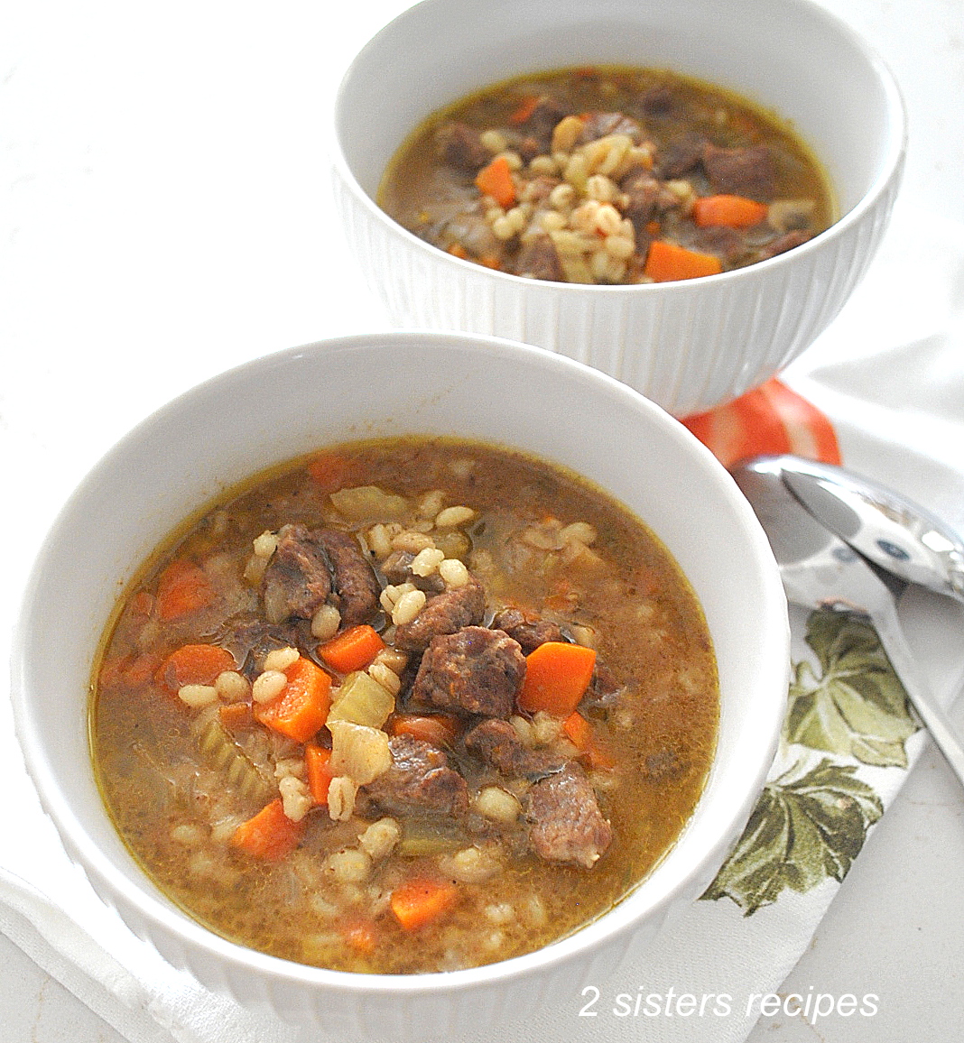 Two white bowls filled with a beef barley vegetable soup.