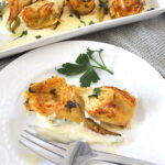 A plate with 2 seared artichokes over some cheese cream and a fork on the plate.