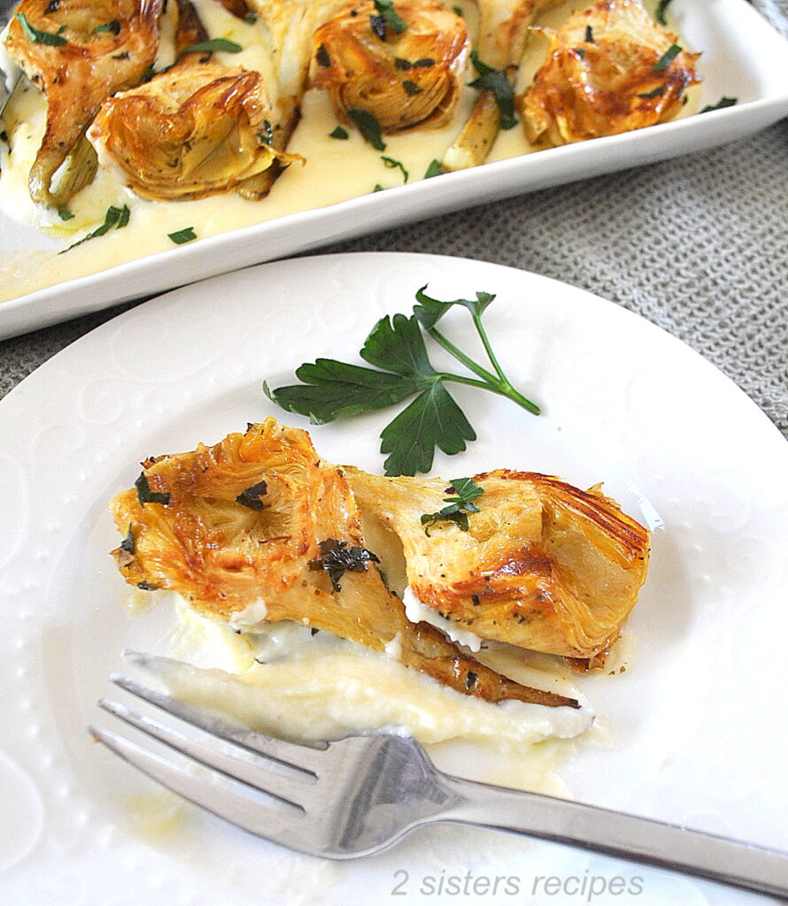 A plate with 2 seared artichokes over some cheese cream and a fork on the plate.