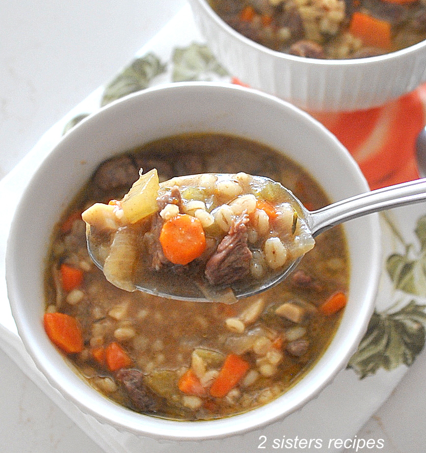 A spoonful of beef barley vegetable soup from white bowl.