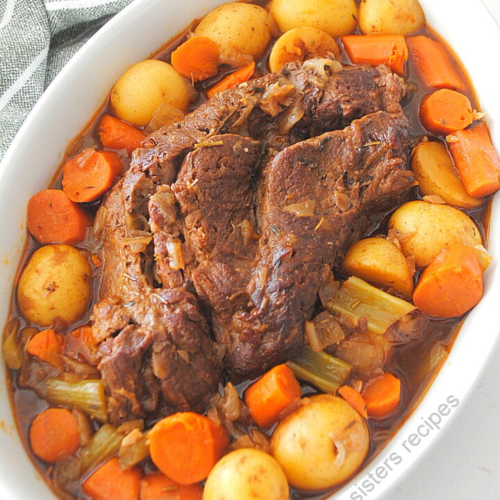 A pot roast served in a white platter with veggies around the roast.