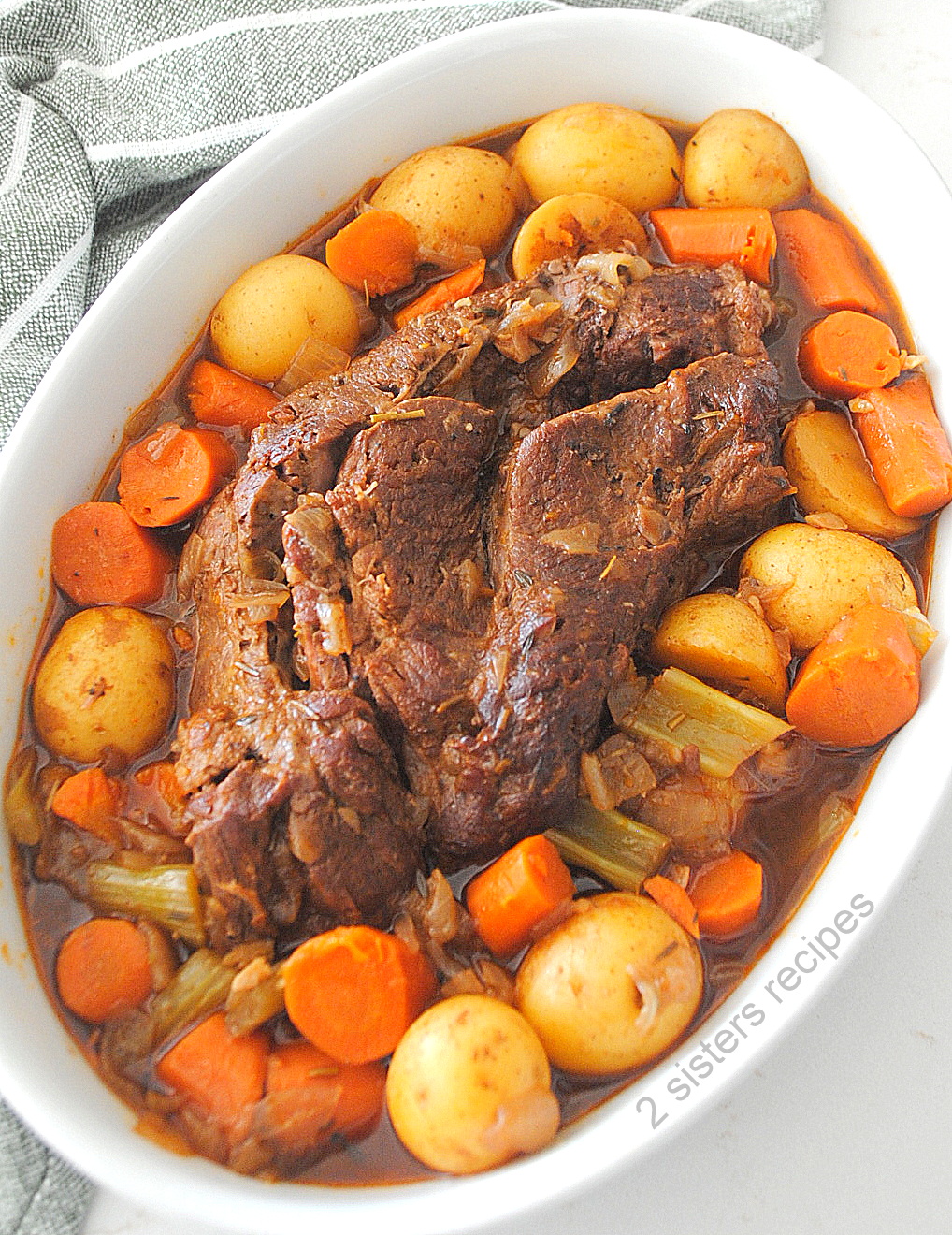 A pot roast served in a white platter with veggies around the roast.