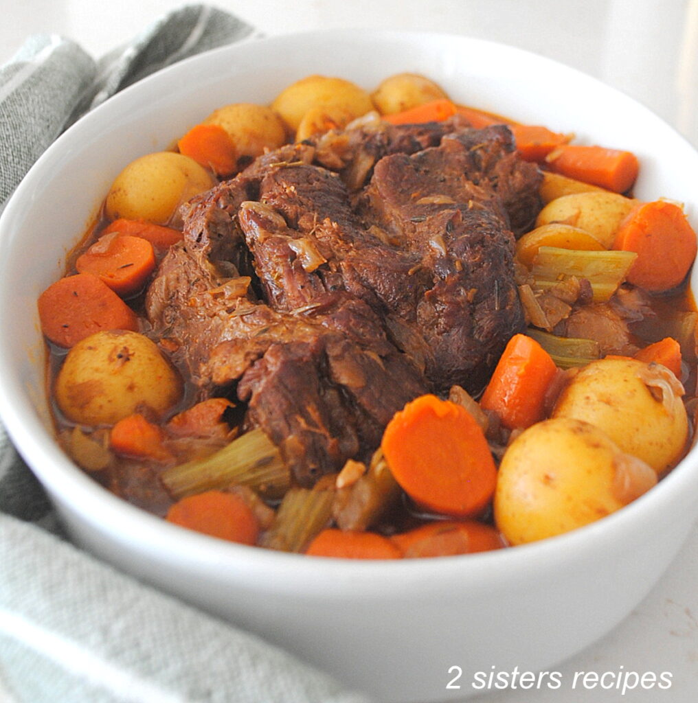 A serving dish filled with cooked pot roast with carrots and potatoes around the roast.