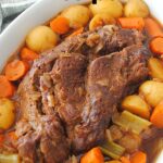 A white dish filled with a cooked pot roast with mixture of vegetables.