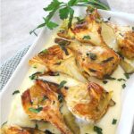 Seared artichokes served on a layer of cream on a rectangular platter with fresh parsley on the side.
